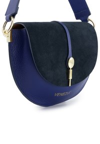 Niebieska torba o zaokrąglonym kształcie, wykonana ze skóry i zamszu. Posiada złote zapięcie oraz teksturowaną powierzchnię. Oznaczona napisem "VENEZIA."