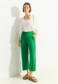 Zielone, szerokie spodnie z elastycznym paskiem, w połączeniu z białym topem na ramiączkach i lekką białą koszulą. Całość dopełniają brązowe sandały.