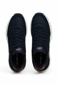 Granatowe sneakersy z tekstylnym i zamszowym wierzchem, białą gumową podeszwą i czerwonymi akcentami wewnętrznymi. Posiadają sznurowadła oraz logo na języku i wkładce.