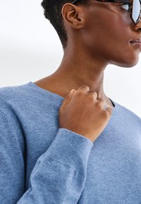 Jasnoniebieski sweter z miękkiego dzianiny z dekoltem w kształcie litery V. Posiada prążkowane mankiety i dół, gładką fakturę oraz minimalną ilość szwów.