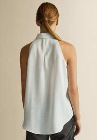 Blusa senza maniche blu chiaro con colletto alto, dettaglio di piega sul retro e orlo arrotondato, realizzata in un tessuto leggero e texturizzato.