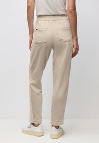 Kvinna som bär beige kordflöjlsbyxor med elastisk midja och bakfickor, tillsammans med vita sneakers.