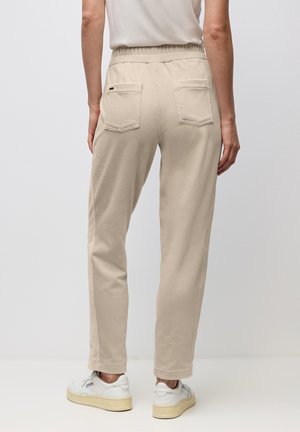 Kvinna som bär beige kordflöjlsbyxor med elastisk midja och bakfickor, tillsammans med vita sneakers.