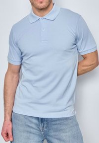 Polo shirt bleu clair à manches courtes avec un col classique, une patte de boutonnage à deux boutons et une texture lisse et légèrement extensible.