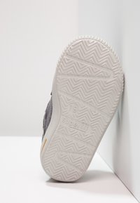 Sole di scarpa grigia per bambini con motivo di battistrada a zigzag e branding "superfit", posizionata su uno sfondo bianco in un angolo.