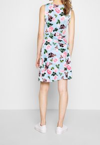 Robe fleurie avec un fond bleu clair, ornée de roses roses et de feuilles vertes. Design sans manches, longueur genoux, associée à des baskets blanches.