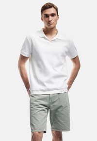 Weißes, geripptes Polohemd mit Kragen, kombiniert mit hellgrünen Shorts. Das Hemd hat eine lockere Passform und ein einfarbiges Design.