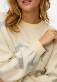 Creme sweater med en blød tekstur, der har et subtilt gråt dyremotiv. Ribbet manchetter og halsudskæring. Lunt, afslappet design.