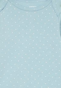 Helles blauen Kurzarm-Overalls aus weicher Baumwolle, mit kleinen weißen Punkten und einem runden Halsausschnitt mit genähtem Rand.