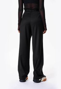 Zwarte wijde broek met hoge taille, gladde textuur en net gesneden ontwerp, gecombineerd met zwart-witte sneakers.