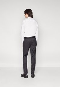 Camisa branca de colarinho e calças escuras com um corte slim. A camisa tem punhos com botões, enquanto as calças apresentam bolsos traseiros e uma textura suave.