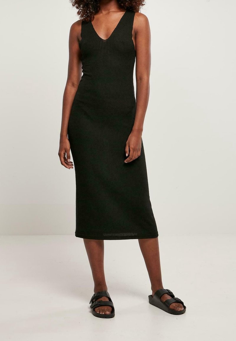 Černé žebrované midi šaty s hlubokým výstřihem ve tvaru V, přiléhavý střih a hladká textura. Nosiče s černými plochými sandály. Jednoduchý, ležérní styl.