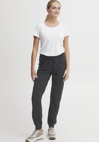 Sorte joggebukser med elastisk linning og snøring, kombinert med en tett hvit t-skjorte og lyse joggesko. Enkelt design.