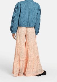 Veste bomber bleue matelassée avec des manches volumineuses et des broderies géométriques, associée à un pantalon large à fleurs pêches fluides avec des détails froncés.