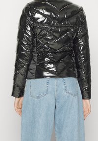 Czarna, błyszcząca kurtka puchowa z chevronowym pikowaniem, długimi rękawami i krótkim krojem, połączona z jasnoniebieskimi dżinsowymi spodniami.