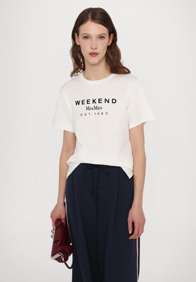 Weißes, kurzärmliges T-Shirt mit schwarzem Text "WEEKEND MaxMara EST. 1983" auf der Vorderseite. Kombiniert mit dunkelblauen Hosen und einer roten Clutch.