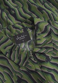 Camicia a maniche lunghe verde e nera con un colletto. Presenta linee ondulate e strisce, realizzata in un tessuto leggero. Etichetta del marchio visibile.