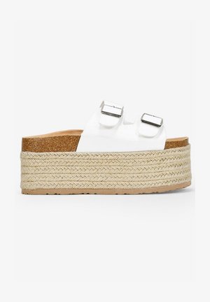 Sandalias de plataforma blancas con dos hebillas plateadas ajustables, media suela de yute trenzado y plantilla de corcho, que presenta una suela de goma plana texturizada.