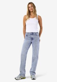 Ανοιχτό μπλε ψηλόμεσα τζιν με ίσια γραμμή, συνδυασμένα με ένα λευκό ριμπ μπλουζάκι και γκρι αθλητικά παπούτσια με πράσινες λεπτομέρειες.