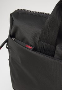 Rucsac negru cu un exterior din nailon texturat, cu un capac cu fermoar, două mânere și un stilou vizibil într-un buzunar frontal.