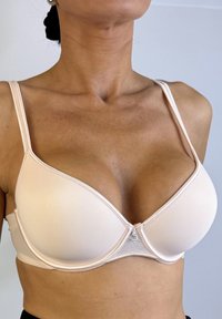 Sostén con aros color beige, con copas moldeadas y suaves, tirantes ajustables y cierre de gancho en la parte posterior. Presenta costuras decorativas a lo largo de los bordes.