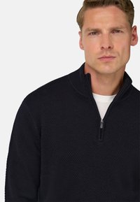 Granatowy sweter dzianinowy z teksturowanym wzorem, z półzamkiem przy kołnierzu i widoczną białą warstwą wewnętrzną przy szyi.