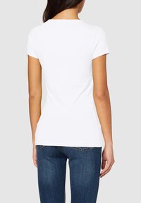 T-shirt blanche à manches courtes avec un col rond, design ajusté et texture lisse, associé à un jean en denim bleu foncé.