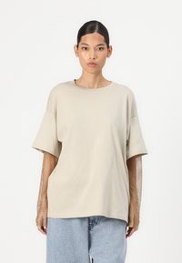 Beige oversized t-shirt met korte mouwen, met geperforeerde mouwen. Gecombineerd met lichtgewassen losse denim shorts. Soepele stoftextuur.