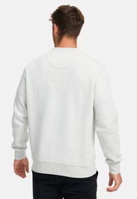 Sudadera gris claro con cuello redondo, puños y bajo acanalados. Textura suave, diseño minimalista, con un acento circular en la parte posterior del cuello.