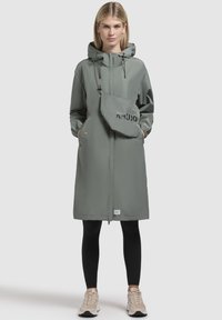 Impermeabil ușor, lung, de culoare verde măsliniu, cu glugă, fermoar și buzunare frontale. Include o geantă de umăr detașabilă cu logo. Material texturat.