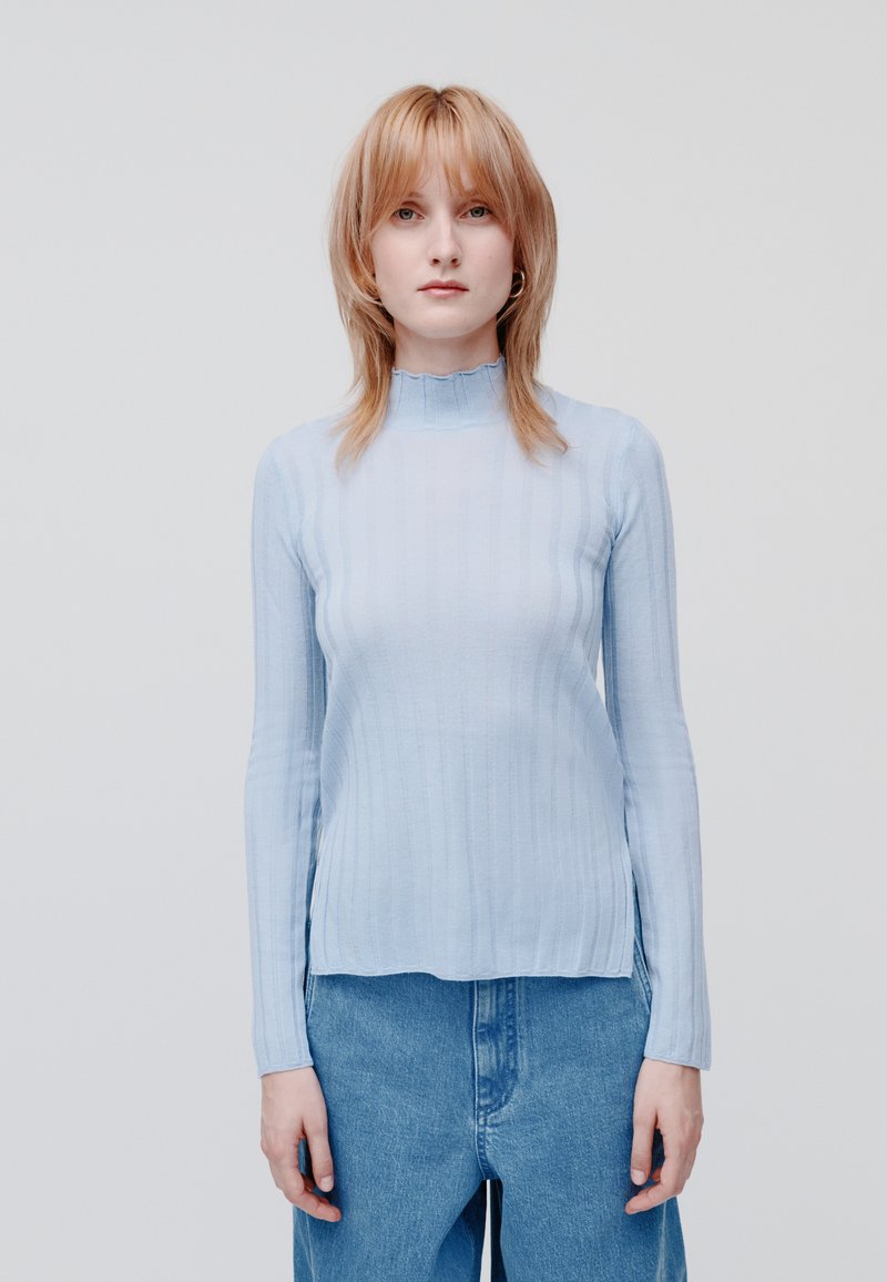 Top azzurro chiaro a maniche lunghe con scollo alto e ondulato, dal morbido tessuto e design aderente, abbinato a pantaloni corti di denim azzurro chiaro.