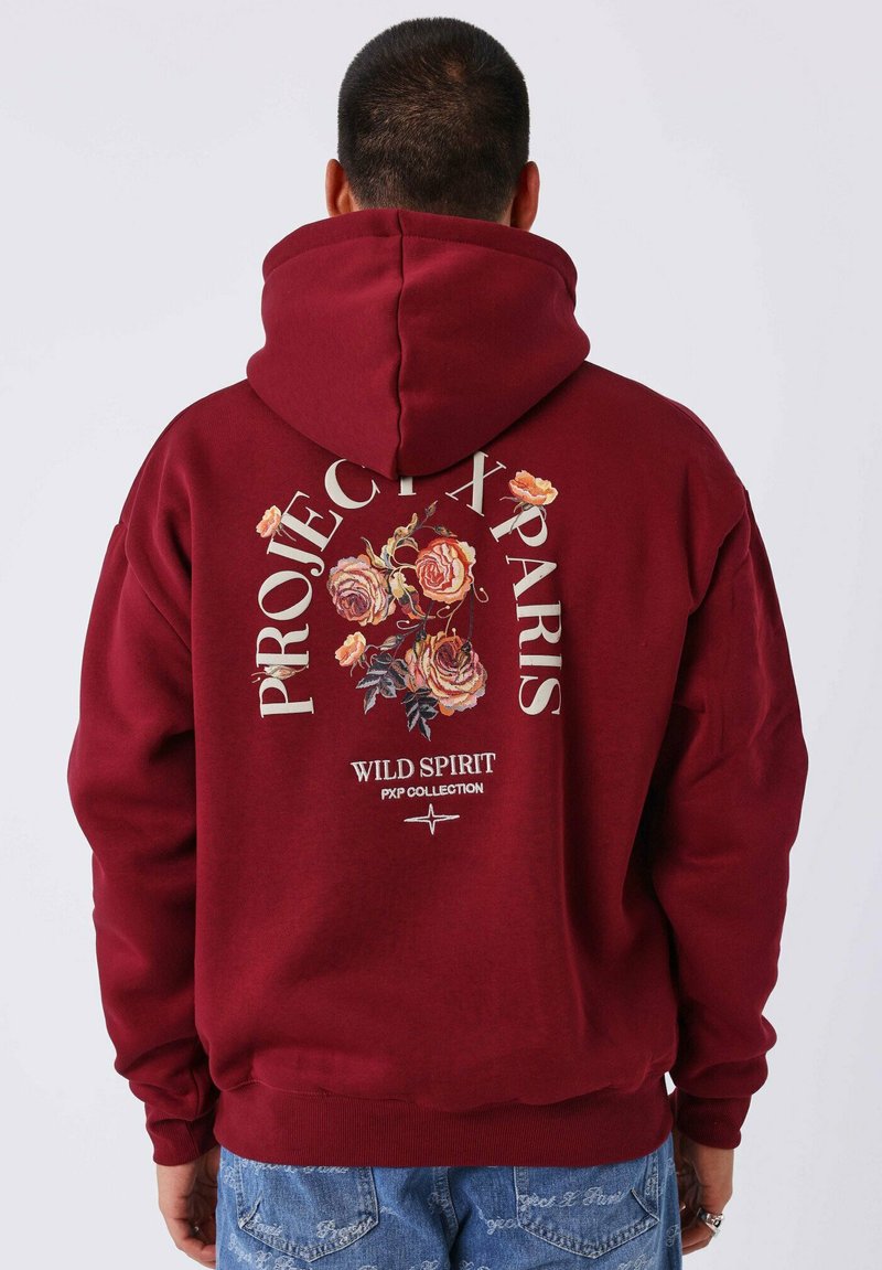 Sudadera color marrón rojizo con un gran gráfico floral en la parte trasera. Presenta el texto "PROJECT X PARIS" y puños y dobladillo acanalados. Textura de tela suave.