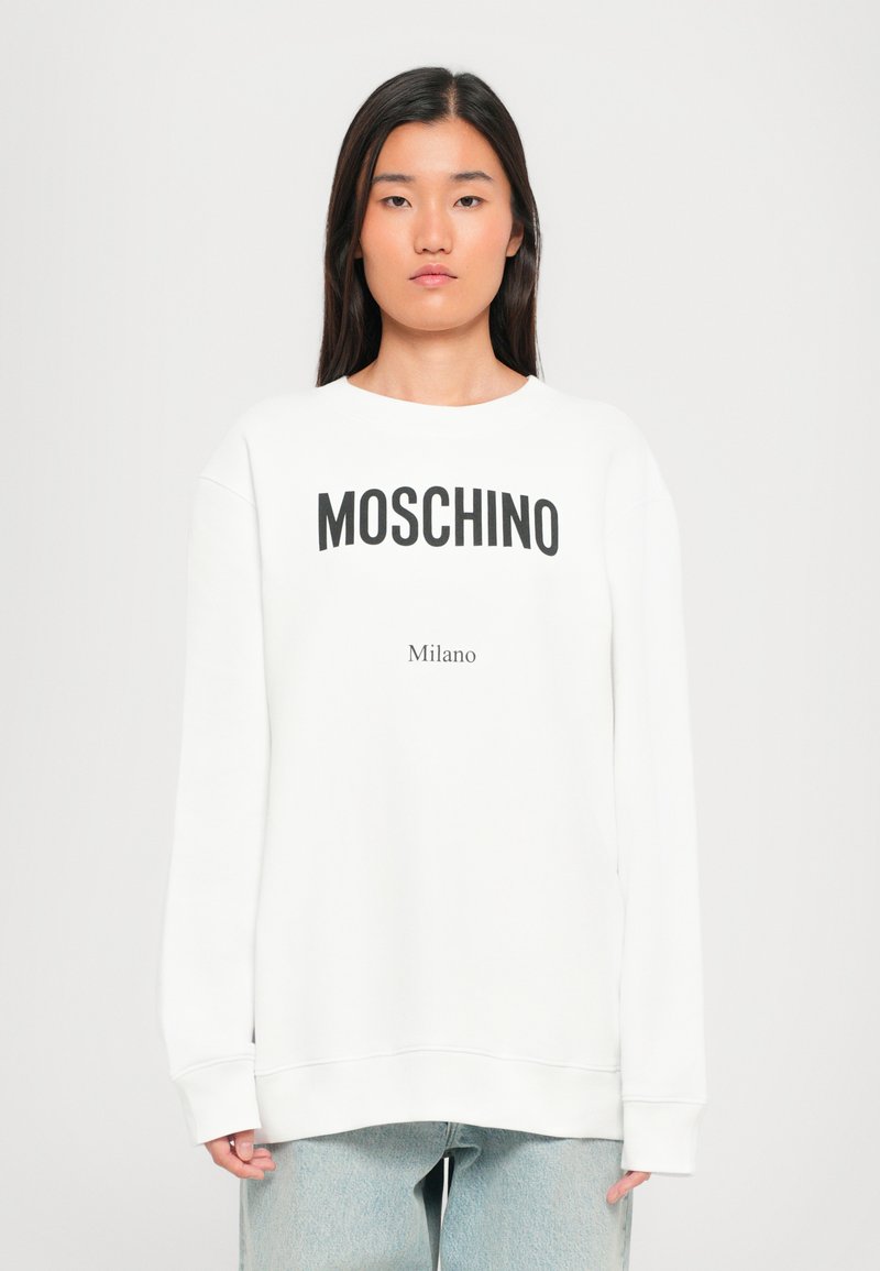 Vit sweatshirt med "MOSCHINO" och "Milano" tryckt i svart. Har långa ärmar, rundad hals och en avslappnad passform. Slät textur.