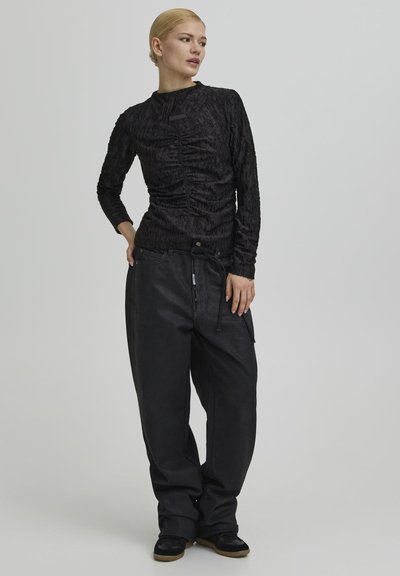 Fekete texturált hosszú ujjú felső összegyűrt anyagmintával; laza fekete nadrággal párosítva, melynek derékrészén húzózsinór és oldalzsebek találhatók.