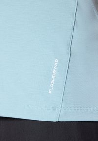  Lichtblauwe performance shirt met een gladde textuur, gestikte naden en een wit "FLASHDRY-XD" logo aan de zijkant.