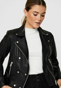 Svart läderbikerjacka med quiltat axeldetalj, silverhardware, asymmetrisk dragkedjestängning och tryckknappsdetaljer.