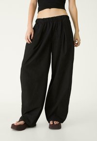 Schwarze, weit geschnittene Hosen aus weichem Stoff mit einem gesmokten elastischen Bund. Sie verfügen über tiefe Seitentaschen und einen lockeren Sitz.