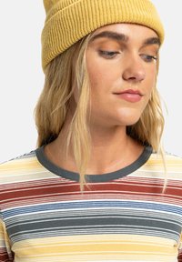 Gestreept ribbelshirt met gele, rode, blauwe en grijze horizontale strepen; grijze kraag; gedragen met een gele gebreide beanie.