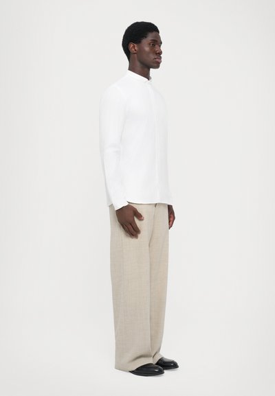 Witte overhemd met lange mouwen en een Chinese kraag, gecombineerd met lichtbeige wijde broek en zwarte schoenen. Eenvoudig, op maat gemaakt ontwerp.