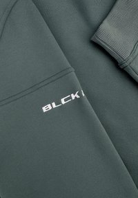 Donkergroene sweatshirt met ribgebreide manchetten en geborduurd "BLCK" logo in het wit op de mouw. Gladde textuur met minimale ontwerpelementen.