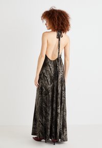 Maxikjole i mørkegrå med teksturert overflate, halterneck og åpen ryggdesign. Har flytende stoff og en elegant silhuett.