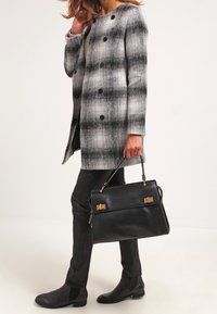Šedý a černý károvaný kabát s knoflíky, černá kožená kabelka se zlatými doplňky, černé přiléhavé kalhoty a černé členkové boty s texturou.
