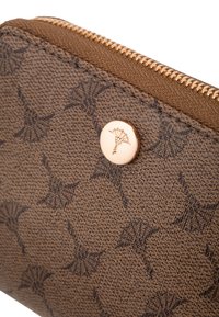 Portafoglio marrone con texture, dotato di una cerniera dorata e di un motivo floreale in rilievo. Sul davanti è visibile un bottone con logo circolare.