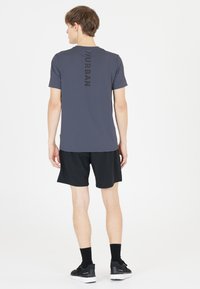 Harmaa urheilusaito, jonka takana on pystysuora musta teksti "URBAN", yhdistettynä mustiin sortseihin ja mustiin lenkkikenkiin, valkoista taustaa vasten.