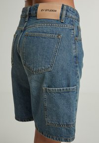 Gaiši zili džinsu šorti ar klasisko piecu kabatu dizainu, ar pastiprinātām šuvēm un ādas etiķeti jostasvietā.