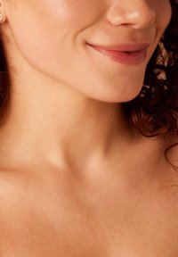 Close-up van de huid van de nek tot de wang, met een gladde textuur en subtiele glans, waarbij krullend haar gedeeltelijk zichtbaar is.