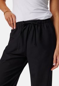 Zwarte elastiche tailleband broek met een koorddetail in de taille. Glad textuur en relaxte pasvorm. Casual ontwerp geschikt voor comfort.