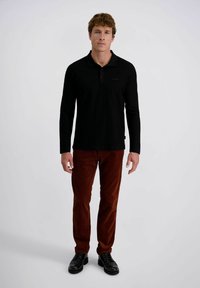 Zwarte langemouwen polo met een knoopkraag, gecombineerd met roodbruine ribfluwelen broek en zwarte schoenen. Eenvoudig ontwerp en gestructureerde stof.