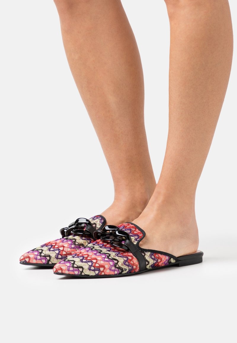 Scarpe slip-on a fantasia con design intrecciato in rosa, rosso e viola, con dettagli neri e un fiocco decorativo sulla parte superiore.