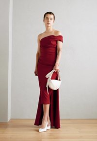 Rochie burgundy ajustată, cu umerii descoperiți și o fenda pe coapsă, împreună cu o geantă albă și tocuri albe cu vârf ascuțit. Textură netedă.